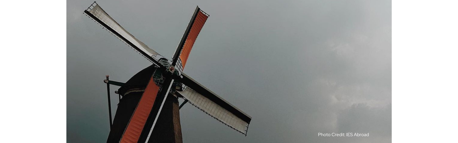 A windmill with two orange blades and two white blades on a cloudy day. 